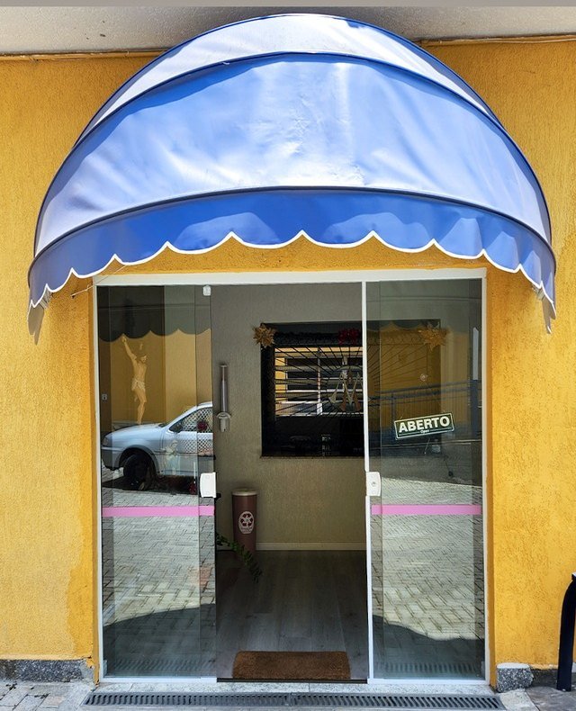Toldo capota azul com acabamento ondulado sobre porta de vidro