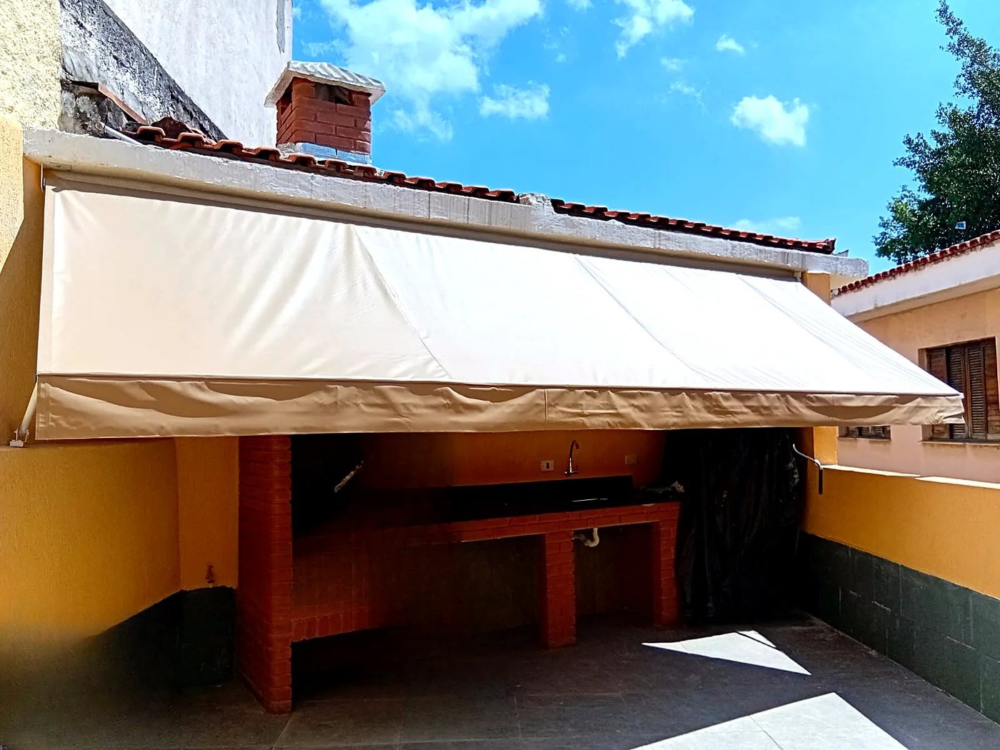 Toldo de lona bege cobrindo a área de churrasqueira de uma casa